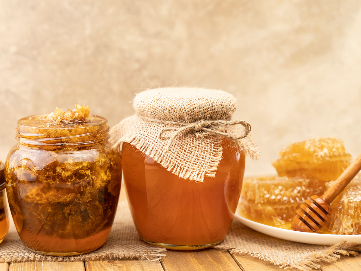 Assortment of honey products: honeycombs, nuts in honey, beeswax in table. Healthy organic honey dipping in jar, closeup. Honey pouring in glass bowl.